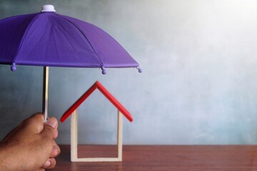 Selective focus image of hand holding umbrella and toy house. House insurance concept.