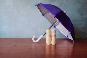 Family insurance concept. Umbrella and wooden dolls with copy space