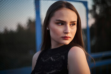 A young attractive woman poses against the backdrop of a mesh fence at sunset. High quality photo