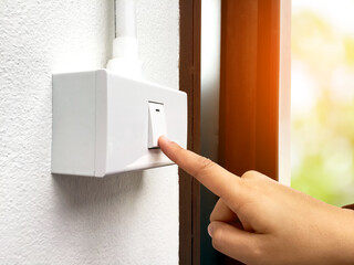 Female home owner is using her hand to turn off the light switch panel on the wall in front of her toilet after using the toilet, soft and selective focus, global warming concept.