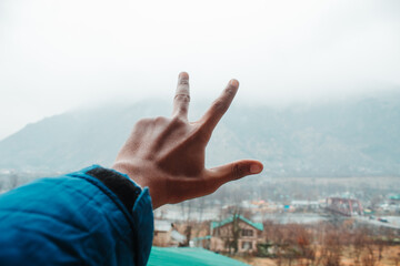Closeup shot of hand of an Indian man making peace sign in front of the mountains at Manali in Himachal Pradesh, India