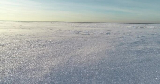 The drone flies over a snowy lake. Shiny snow flies around. The drone hovers over a snowy field. A hovercraft rides on a snow-covered lake.
