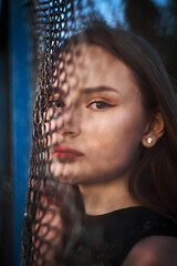 A young attractive woman poses against the backdrop of a mesh fence at sunset. High quality photo
