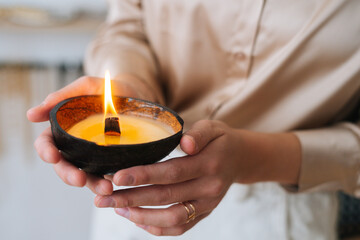 Close-up cropped shot of unrecognizable young woman holding burning scented handmade candle in...