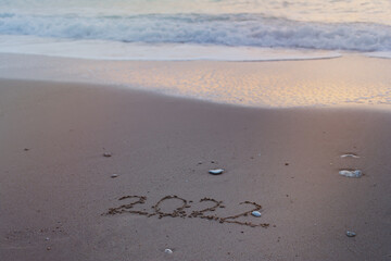 2022 Happy New Year inscription sand beach. The written text is written on yellow sand and is washed away by a wave. The concept of changing the year, the holiday. Mockup postcards copy space