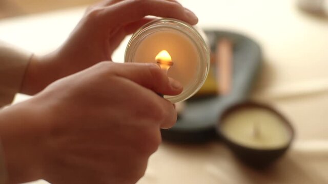 Close-up cropped shot of unrecognizable young woman lighting handmade aroma candle holding in hand. Closeup of female burn up with lighter aroma relaxing candle at home. Shooting in slow motion.