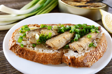 Fish sandwich with sprats, butter and green onion on white plate, close-up