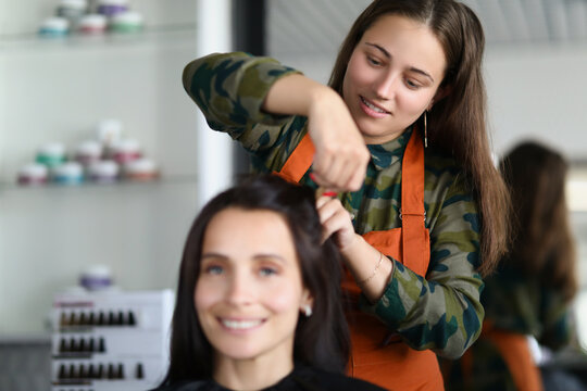Smiling hairdresser creating fancy hairstyle for female client