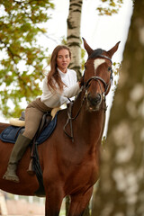 Obraz premium Beautiful brunette on a horse on the background of an autumn landscape. Horseback riding, active horseback riding