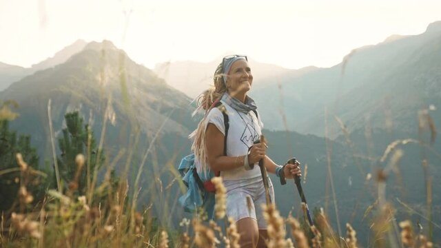 Blonde woman with dreadlocks hiking at sunset smiles, Benasque, Spain, medium shot