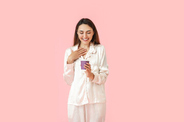 Beautiful woman in pajamas and with cup of coffee on color background