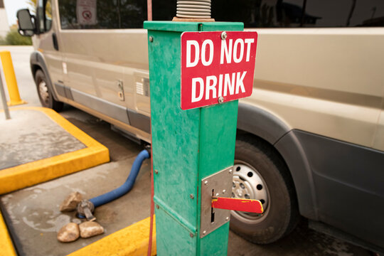 "DO NOT DRINK" sign at RV wastewater dumping station; RV connected and dumping in view