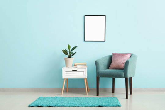 Comfy armchair with table and blank poster on color wall