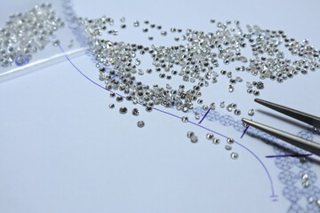Diamonds on white paper with the necklace designed and diamond tweezers. Jewelry maker and designer...