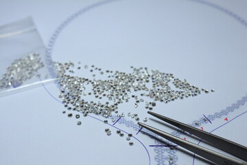 Diamonds on white paper with the necklace designed and diamond tweezers. Jewelry maker and designer concept