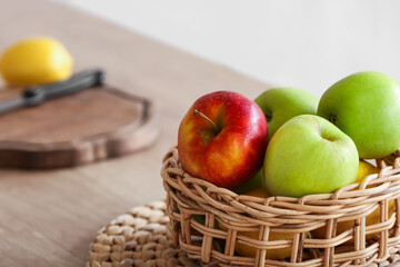 Wicker basket with apples on table in kitchen, closeup