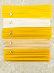 vertical flat top view of various Italian dry pasta on a grey background. wooden letters with the word -pasta.
