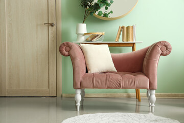 Pink armchair and table with books near green wall