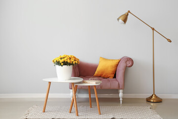 Tables with flowers in pot, book. armchair and lamp near light wall