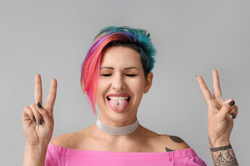 Cool woman with unusual hair showing victory gesture on grey background