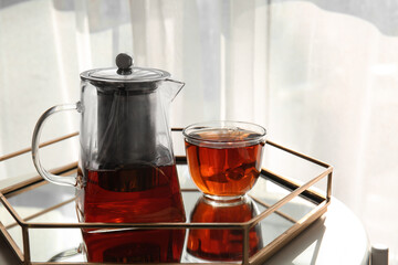 Glass cup of tasty tea and pot on table at home