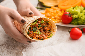 Woman holding tasty burrito on light background, closeup