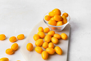 Bowl with tasty kumquat fruits  on light background