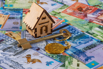 Golden key with a keychain in the form of a coin in denomination of 100 Kazakhstani tenge against the background of Kazakhstani banknotes