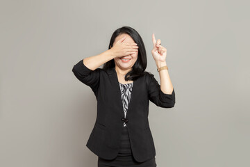 Young woman in black suit is pointing up while covering her eyes with her hands