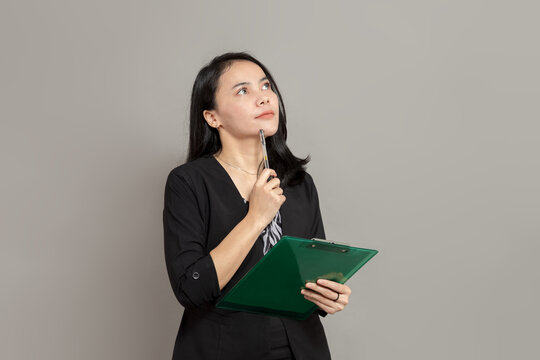 Asian woman is imagining while holding a pen and clipboard