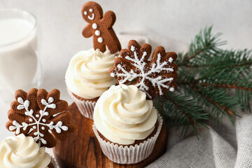 Wooden board of tasty Christmas cupcakes with gingerbread cookies on light background