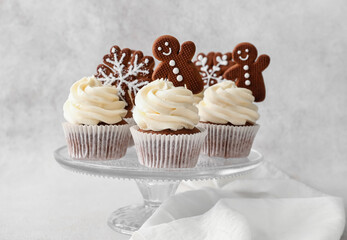 Stand of tasty Christmas cupcakes with gingerbread cookies on light background