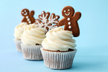 Tasty Christmas cupcakes with gingerbread cookies on blue background