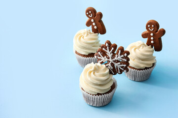 Tasty Christmas cupcakes with gingerbread cookies on blue background