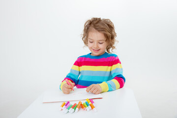 a little cute girl draws at the table with pencils isolated on a white background