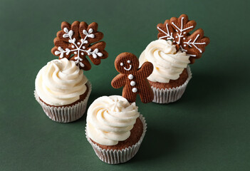 Tasty Christmas cupcakes with gingerbread cookies on green background