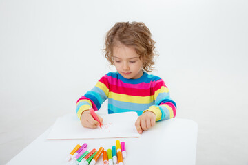 a little cute girl draws at the table with pencils isolated on a white background
