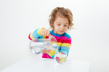 a little cute girl holds a jug of water, pours water into a glass isolated on a white background