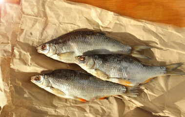 Dried fish for beer on beige paper on a wooden table. River fish top view