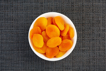 Dried apricots in a white plate on a dark background view from above