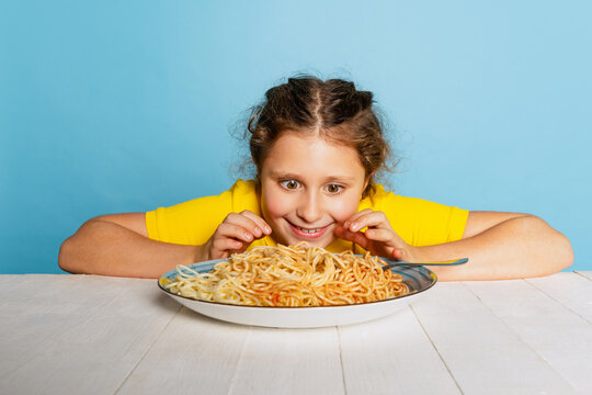 Cute Little Girl, Emotive Kid Eating Delicious Italian Pasta Isolated On Blue Studio Background. World Pasta Day