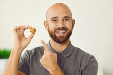 Portrait of confident man with beautiful healthy smile holding walnut in his hand. Close up head shot of young smiling guy pointing his finger at nut showing off his healthy teeth. Dental banner.