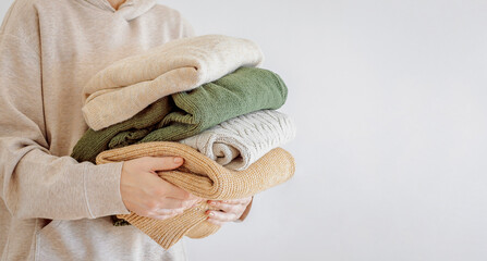 Woman's hand holding a stack of clothes. Clothes Donation, Renewable Concept.Preparing Garment at Home before Donate. Woman packs clothes for a donation or for moving