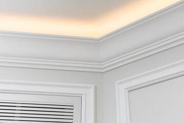 Close-up detail of renovation in modern interior. Angular ceiling skirting made of classic white moldings with built-in LED ceiling lighting. - obrazy, fototapety, plakaty