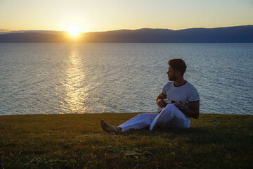 Guy in white clothes with ukulele at sunset