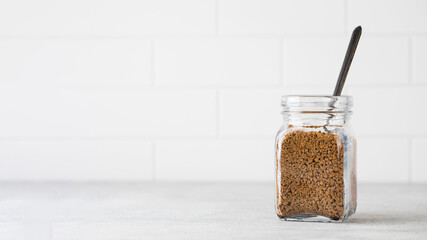 Glass jar with instant coffee with a spoon on a light background. Copy space.