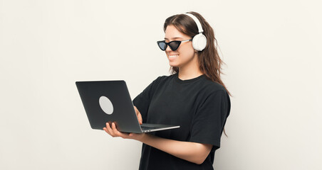 Happy young woman in cool sunglasses, using a laptop and headphones, technology concpet