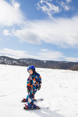 Fototapeta na wymiar kid boy in helmet, winter overalls skiing in the snowy mountains. Winter active entertainment for children. Skiing lesson at an alpine school. Seasonal joys, happy childhood. Sports education