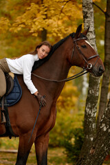 Obraz premium Beautiful brunette on a horse on the background of an autumn landscape. Horseback riding, active horseback riding