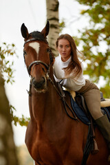 Fototapeta premium Beautiful young woman riding a horse on the field. Sideways to the camera. Freedom, joy, movement